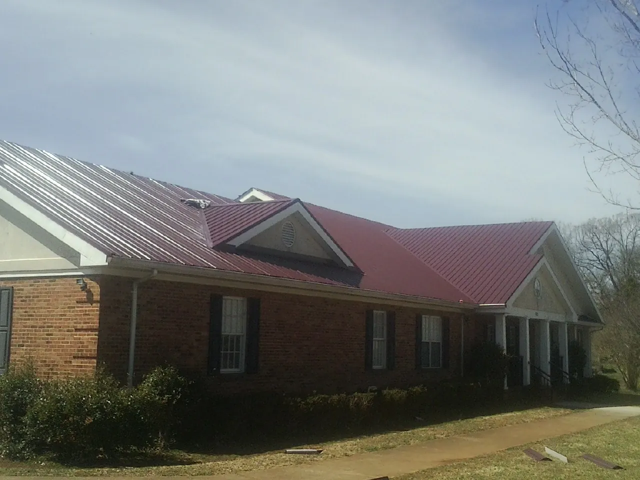 Red metal roof with gabled entries on a long brick building, from a Hail Damage Roof Repair job in Sabillasville