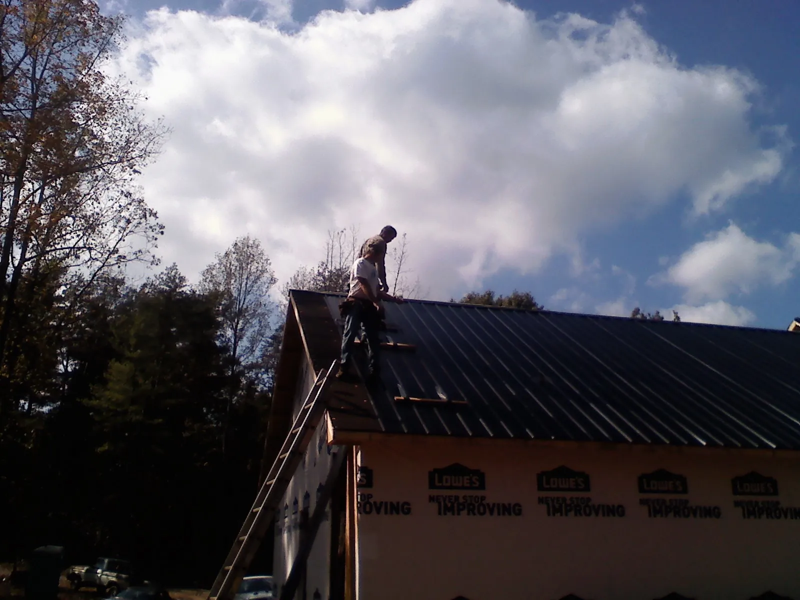 Roofer fastening dark metal panels high against a cloudy sky, from a Roof Inspection job in Sabillasville