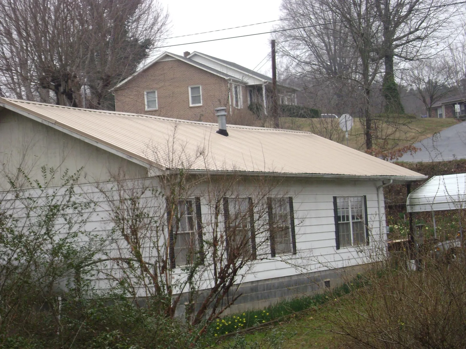 Tan metal roof on a white sided house set into a hillside — Commercial Roofing by Roofing Brothers in Sabillasville